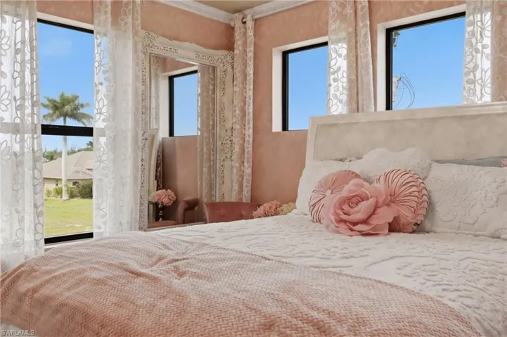 Room featuring multiple windows with natural light, a decorative mirror with an ornate frame, a light-colored headboard, and textured wall finish