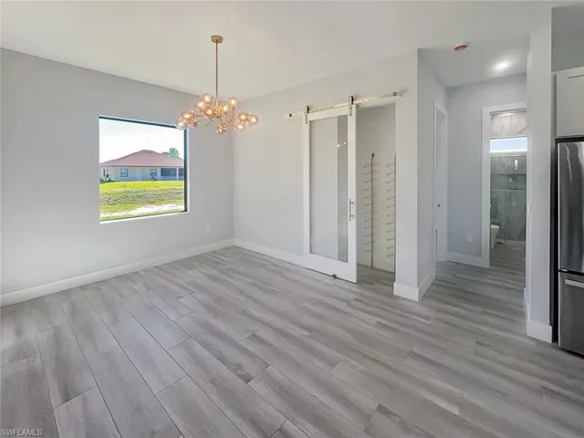 Unfurnished dining area featuring a barn door, light wood-type flooring, and a chandelier