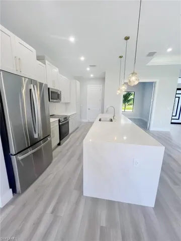 Kitchen featuring appliances with stainless steel finishes, hanging light fixtures, white cabinetry, light stone counters, and recessed lighting