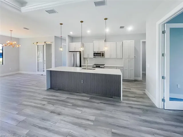 Kitchen featuring stainless steel appliances, white cabinets, a chandelier, light stone counters, and light wood finished floors