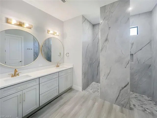 Bathroom with a marble finish shower, double vanity, and light wood-style flooring