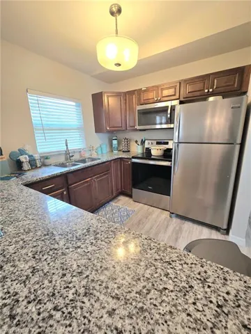 Kitchen featuring appliances with stainless steel finishes, built in microwave,  light wood-style flooring, granite countertops, and decorative light fixtures