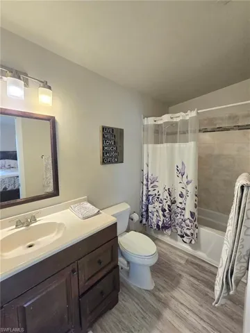 Ensuite bathroom with exterior door to patio with wood finished floors, shower / tub combo, vanity, and toilet including shower curtain and towels
