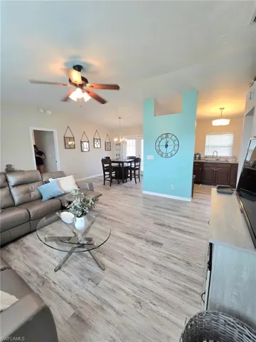 Living room with a chandelier, light wood finished floors, baseboards, and ceiling fan