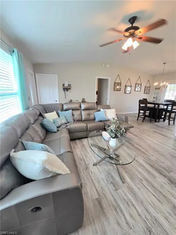 Living room featuring wood finished floors, lighted ceiling fan, vaulted ceiling, with reclining sofa, glass coffee table and window coverings