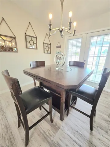 Dining room with expandable table with storage featuring a chandelier, light wood-style flooring, baseboards, and french doors