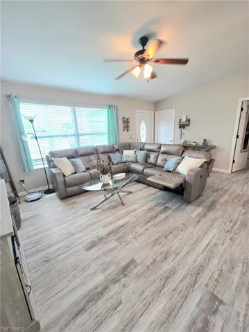 Living area with wood finished floors, a ceiling fan, and baseboards including all furnishings, window coverings, floor lamp and wall decor