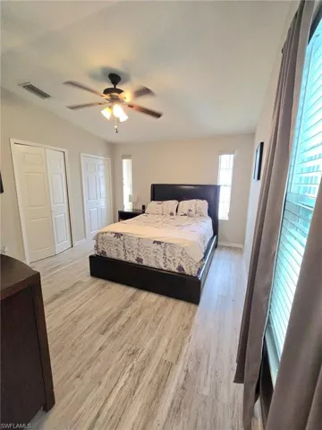 Primary Bedroom with two closets, wood finished floors, baseboards, and a ceiling fan includes bed, nightstand, dresser, window coverings and bedding.