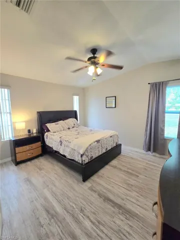 Bedroom with light wood-type flooring, baseboards, vaulted ceiling, and a ceiling fan including all furniture, bedding and window coverings