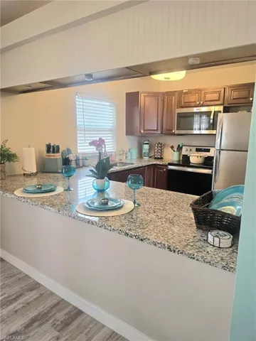Kitchen featuring stainless steel appliances, light stone countertops, light wood-style floors, and brown cabinetry, fresh paint throughout, room for bar seating.