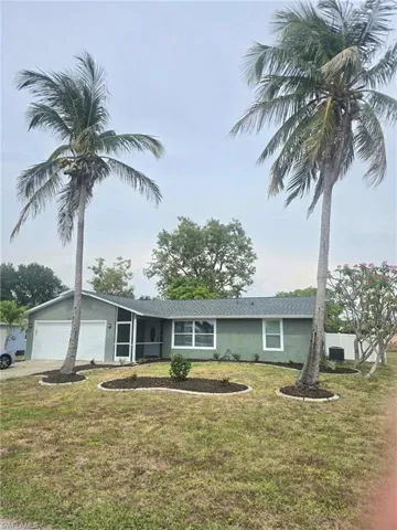 View of front of house with driveway, a front yard, stucco siding, and an attached garage with curbed planting beds featuring mature coconut palms