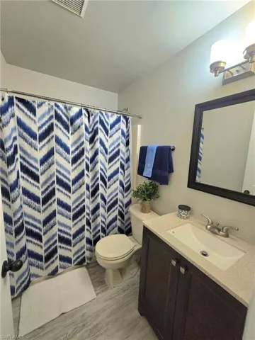 Guest Bathroom featuring tub shower combo,  wood finished floors, toilet, vanity, including shower curtain and towels