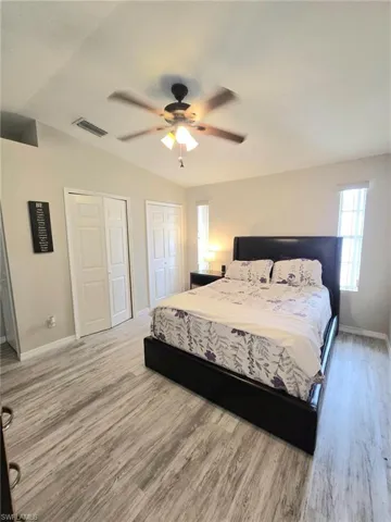 Bedroom with multiple closets, baseboards, wood finished floors, vaulted ceiling, and ceiling fan