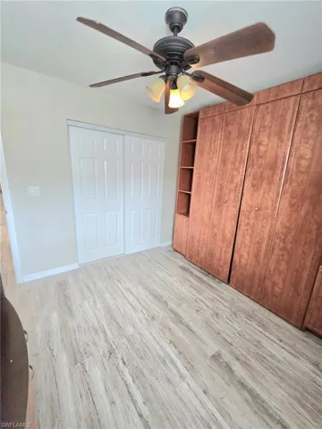 Guest bedroom #2 featuring Wall cabinet with Murphy Pull down queen size bed wood finished floors, a ceiling fan, baseboards, and a closet