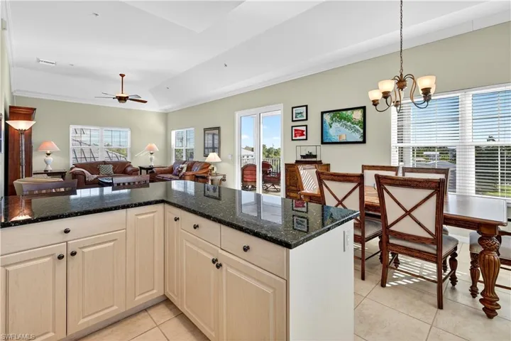 Kitchen featuring dark stone countertops, open floor plan, ornamental molding, light tile patterned floors, and hanging light fixtures