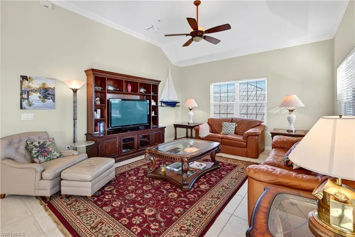 Living area with ornamental molding, healthy amount of natural light, vaulted ceiling, light tile patterned floors, and ceiling fan