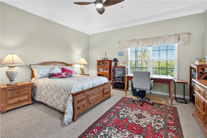 Bedroom featuring light colored carpet, ornamental molding, ceiling fan, and an office area
