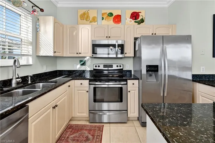 Kitchen with appliances with stainless steel finishes, crown molding, dark stone counters, and light tile patterned floors