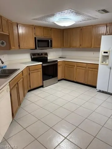 Kitchen featuring light countertops, stainless steel appliances, light tile patterned flooring, and wood finish cabinetry