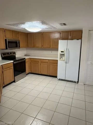 Kitchen with stainless steel appliances, light countertops, light tile patterned floors, and wood finish cabinetry