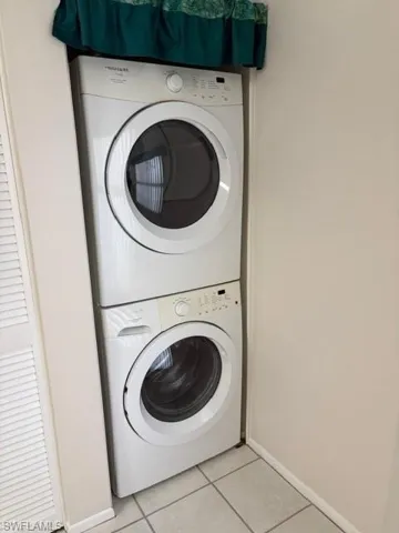 Laundry area with stacked washer / drying machine and light tile patterned floors