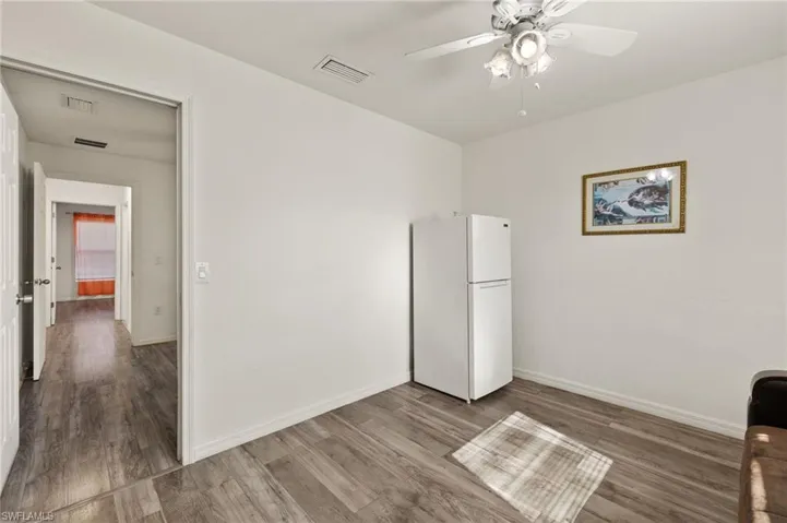 Unfurnished bedroom with ceiling fan, a closet, white fridge, and wood-type flooring