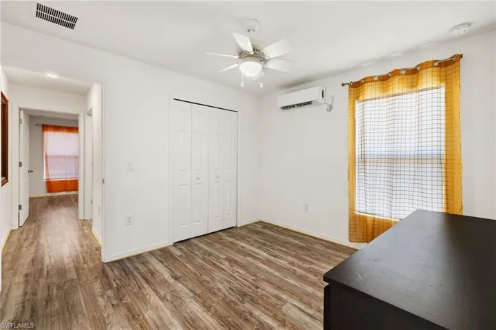 Bedroom featuring hardwood / wood-style flooring, ceiling fan, a wall unit AC, and a closet