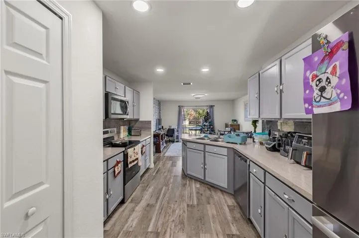 Kitchen featuring gray cabinets, light wood-type flooring, appliances with stainless steel finishes, and tasteful backsplash