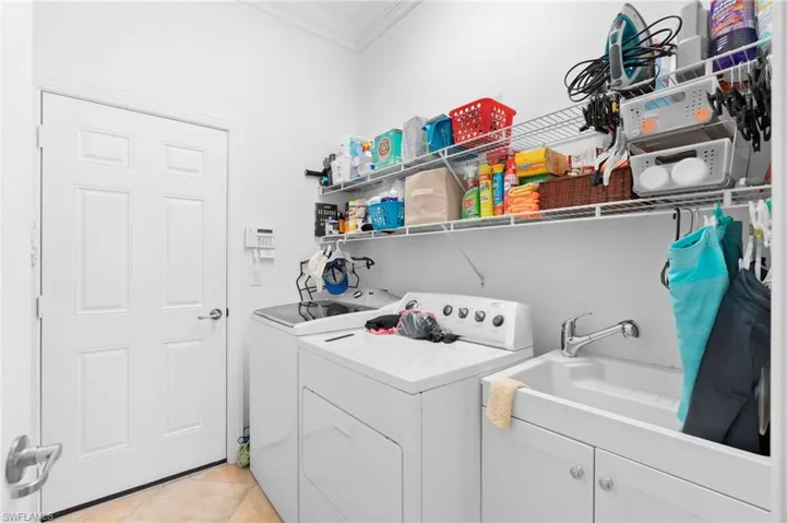 Laundry area with independent washer and dryer, crown molding, light tile patterned floors, and cabinet space