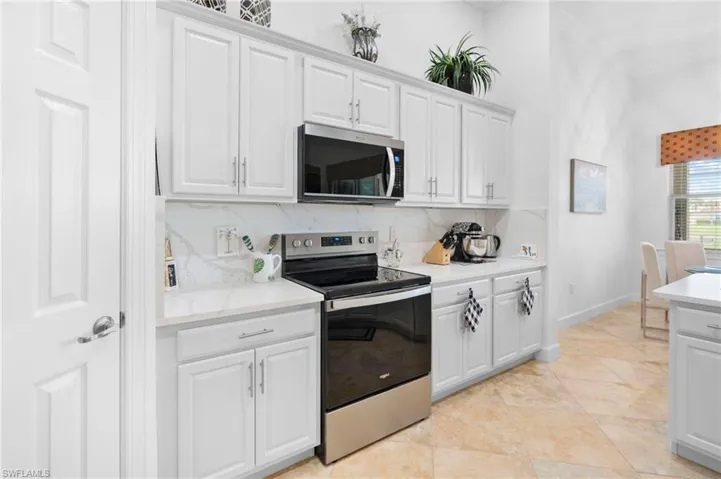 Kitchen with stainless steel appliances, decorative backsplash, light countertops, and white cabinetry