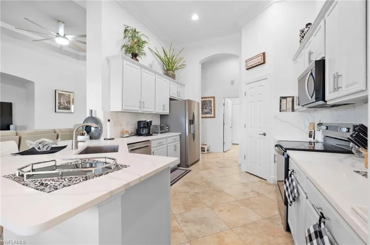 Kitchen featuring ornamental molding, stainless steel appliances, decorative backsplash, arched walkways, and white cabinets