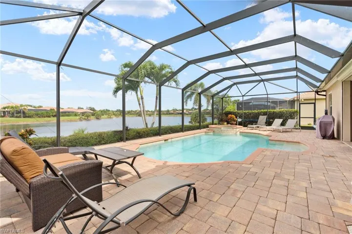 View of pool featuring a patio, a water view, glass enclosure, a pool with connected hot tub, and grilling area