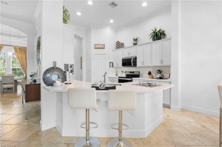 Kitchen with ornamental molding, decorative backsplash, a kitchen bar, appliances with stainless steel finishes, and light countertops