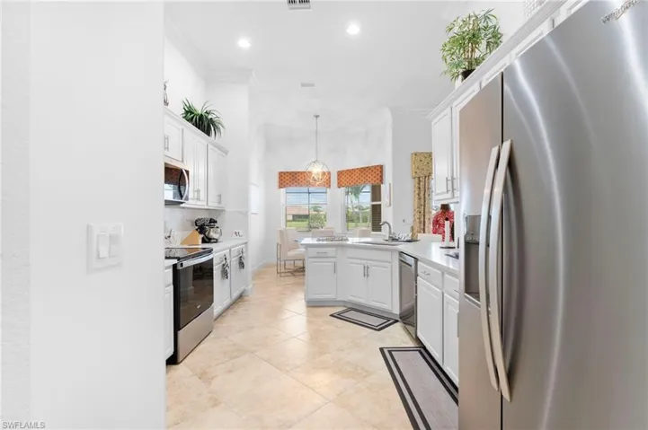 Kitchen with stainless steel appliances, a peninsula, white cabinetry, crown molding, and light countertops