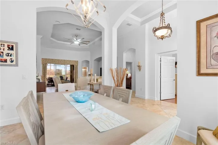 Dining room featuring arched walkways, a high ceiling, a tray ceiling, a chandelier, and light tile patterned flooring