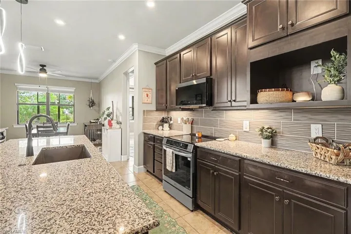Kitchen featuring dark wood cabinetry, an expansive stone-surface island with an integrated undermount sink, stainless steel appliances, and horizontal tile backsplash