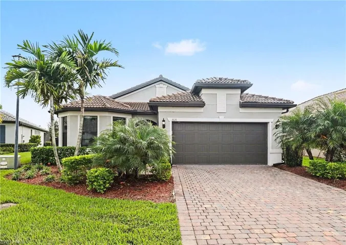 Single-story residence featuring a tile roof, stucco exterior, paved brick driveway, and mature landscaping