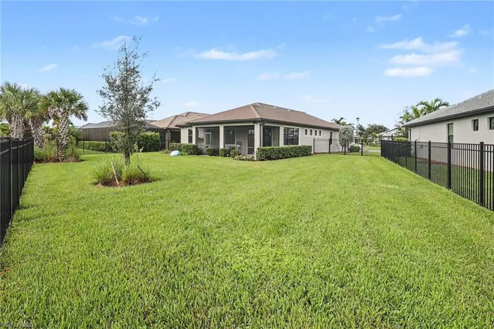 Expansive backyard featuring a manicured lawn, black metal perimeter fencing, a screened-in lanai, and mature palms