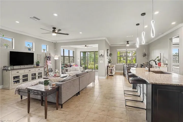 Open-concept living space featuring large-format tile flooring, recessed ceiling lighting, a curved kitchen island with stone countertops, modern pendant lighting, and sliding glass doors