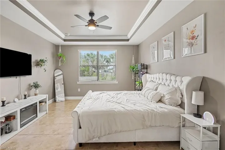 Tray ceiling with crown molding, ceiling fan, tile flooring, and integrated wall-mounted electric fireplace