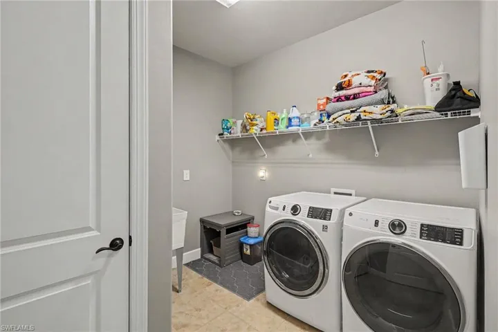 Laundry area featuring tile flooring, white utility sink, and wall-mounted wire shelving