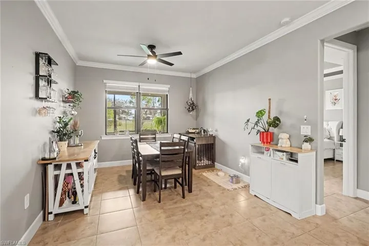 Neutral-toned interior space featuring ceramic tile flooring, crown molding, a multi-blade ceiling fan with integrated lighting, and a window with blinds