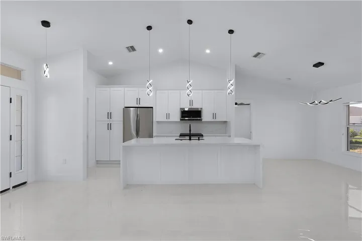 Kitchen featuring appliances with stainless steel finishes, vaulted ceiling, a kitchen island with sink, white cabinets, and hanging light fixtures