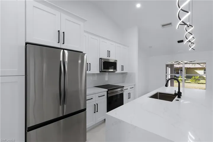 Kitchen with appliances with stainless steel finishes, white cabinetry, lofted ceiling, and sink