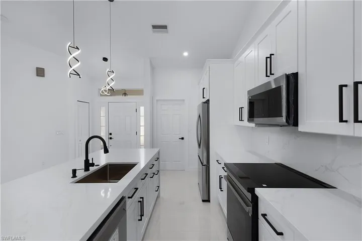 Kitchen featuring appliances with stainless steel finishes, decorative light fixtures, white cabinetry, and sink