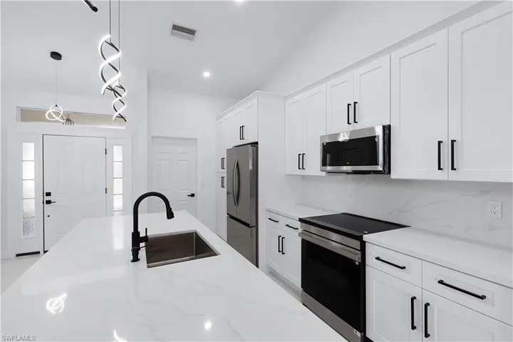 Kitchen featuring hanging light fixtures, light stone counters, sink, and stainless steel appliances