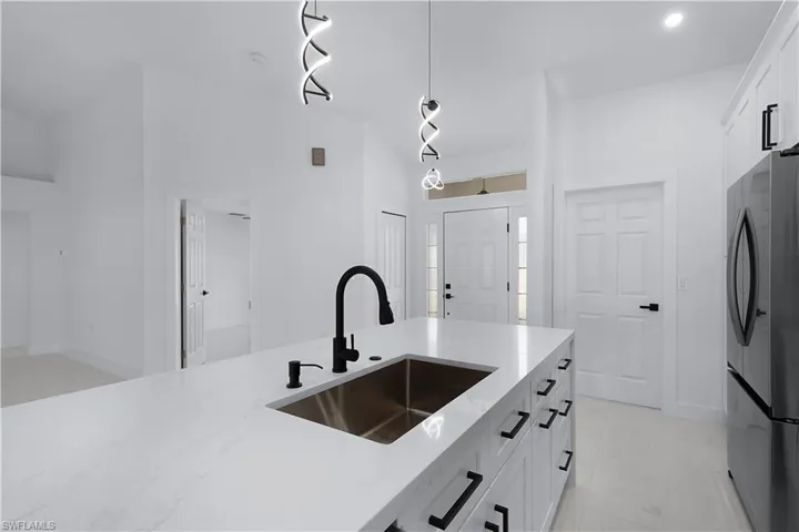 Kitchen featuring stainless steel refrigerator, white cabinetry, sink, and decorative light fixtures