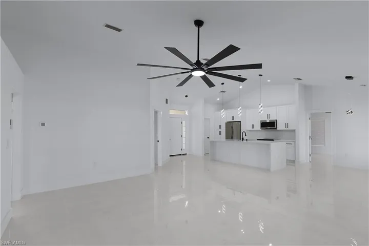 Unfurnished living room with ceiling fan, sink, and high vaulted ceiling