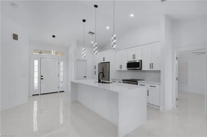 Kitchen with stainless steel appliances, white cabinetry, hanging light fixtures, and an island with sink
