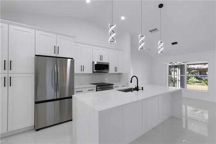 Kitchen featuring white cabinets, sink, hanging light fixtures, vaulted ceiling, and stainless-steel appliances